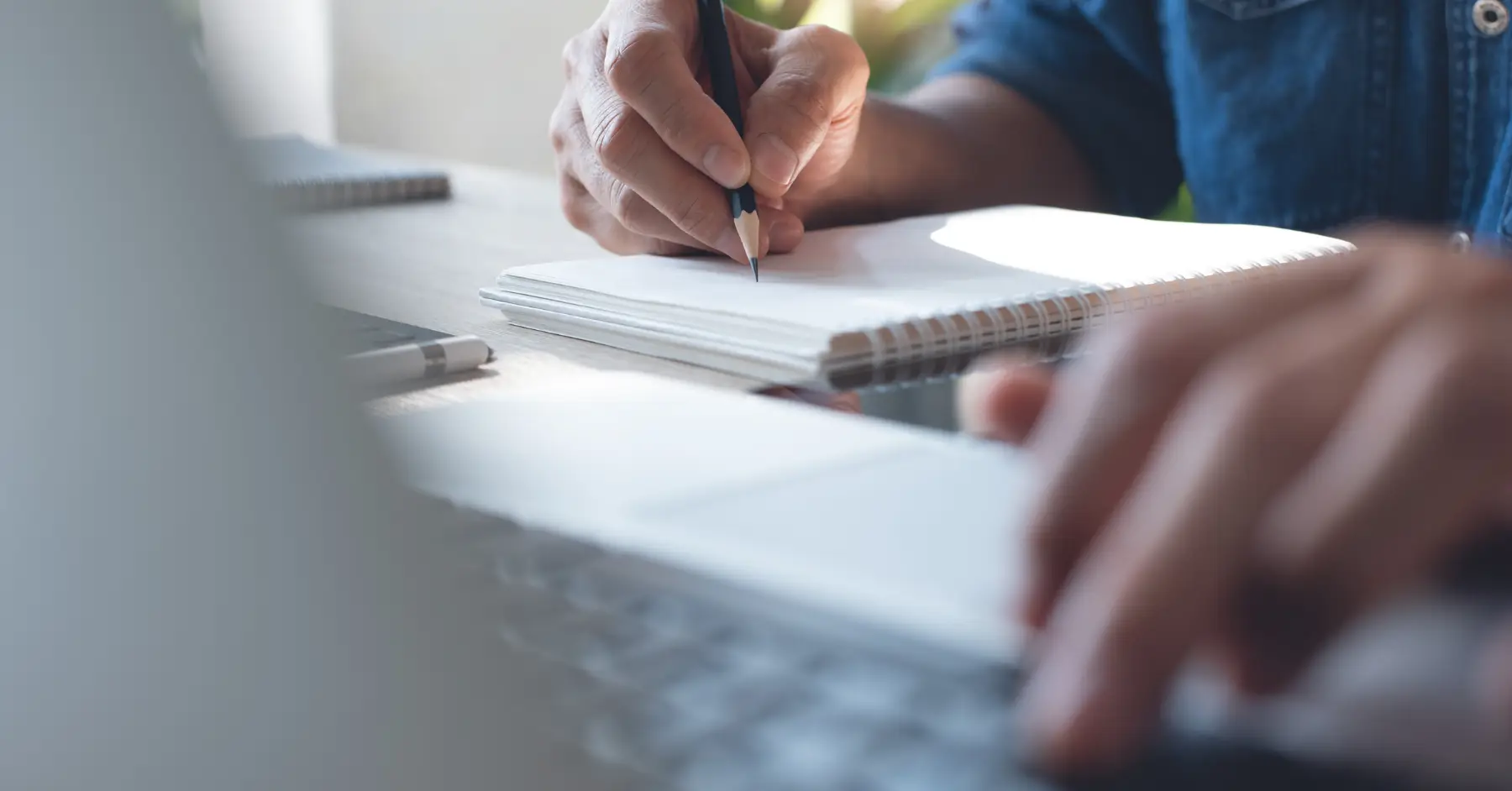 Close-up of a person writing in a notebook beside a laptop, emphasizing focused study and online learning.