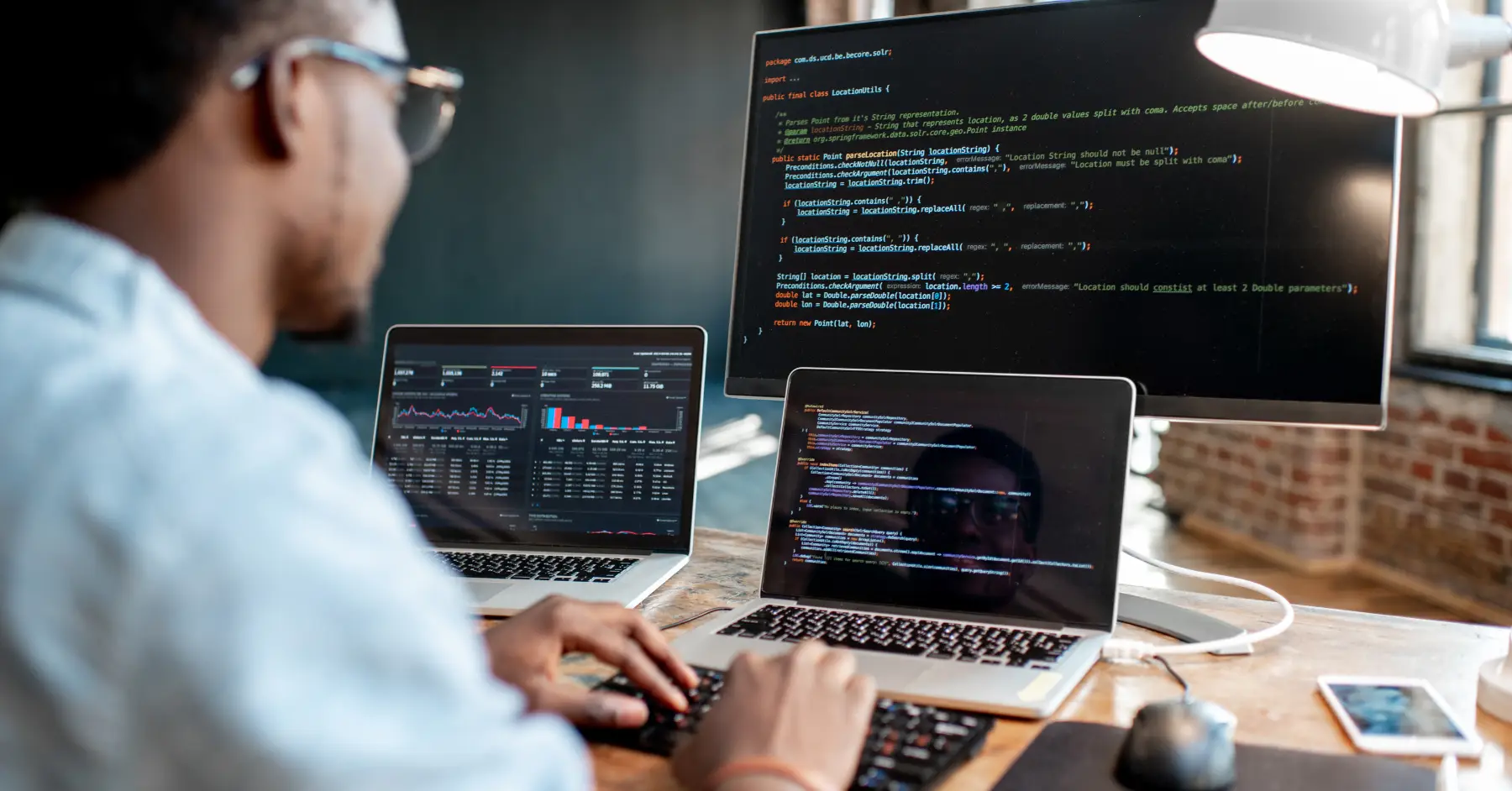A person working on two laptops, displaying coding interfaces with software development code.
