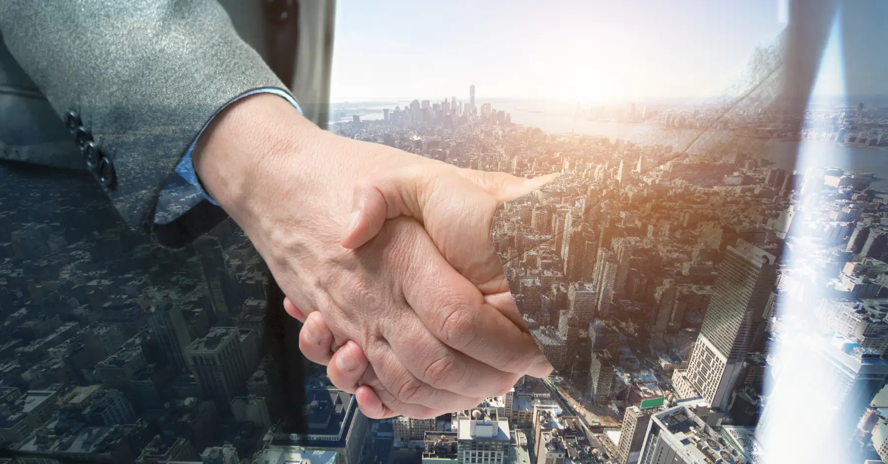 Two business professionals shaking hands, superimposed over a cityscape, symbolizing partnership and venture capital agreements in an urban setting.