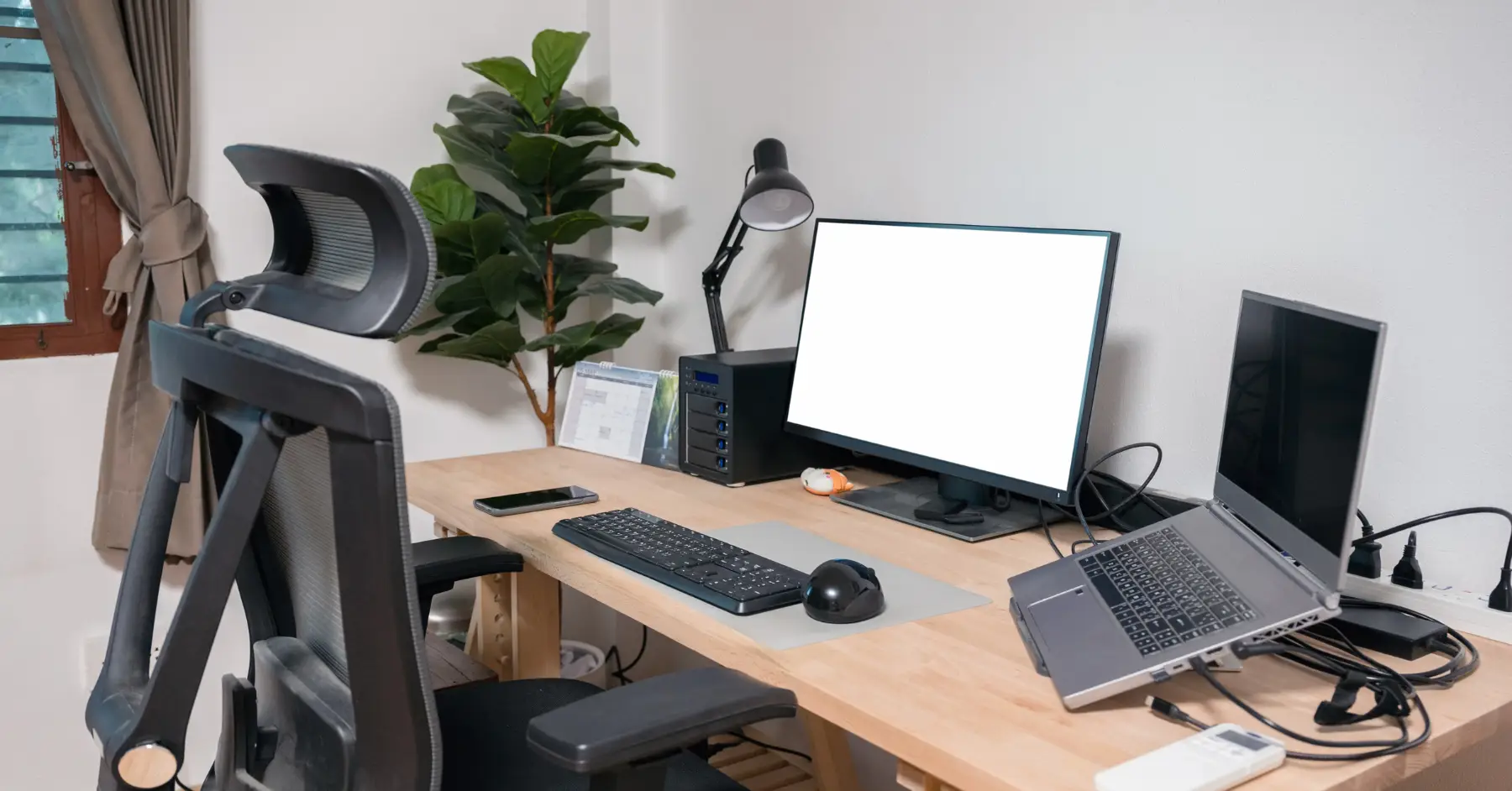 Well-organized home office setup with ergonomic chair, dual monitors, keyboard, and natural lighting.