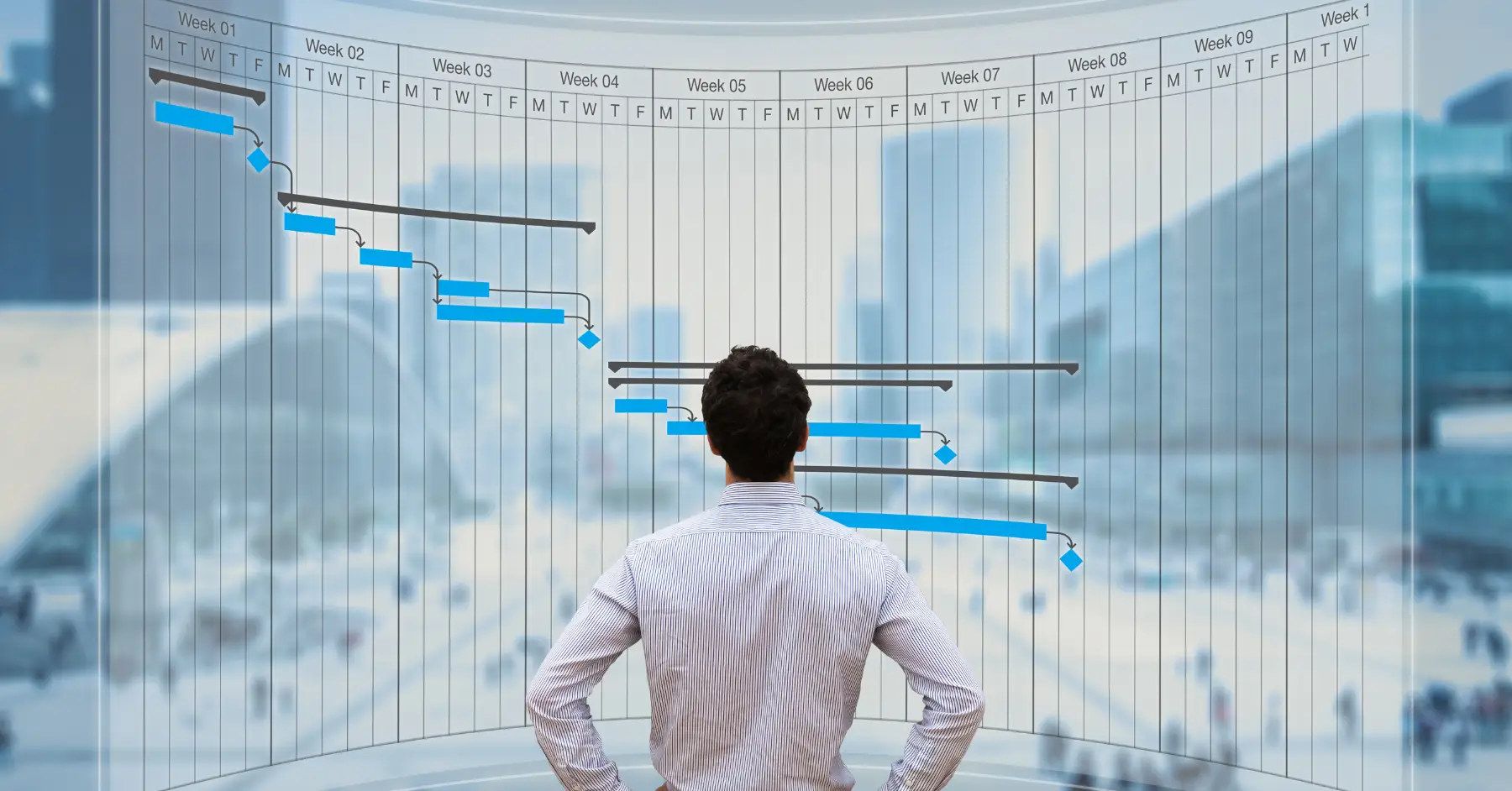 A man stands looking at a Gantt chart projected on a transparent screen, depicting project timelines against a backdrop of a cityscape.