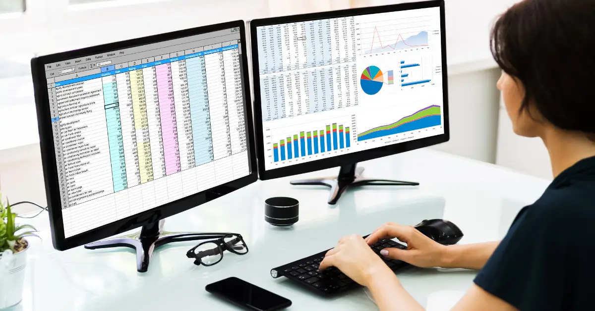 Professional analyzing data using advanced Excel skills on two monitors displaying spreadsheets and charts.