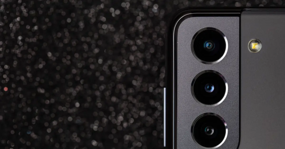Close-up of a modern smartphone's triple camera system against a glittering black background.