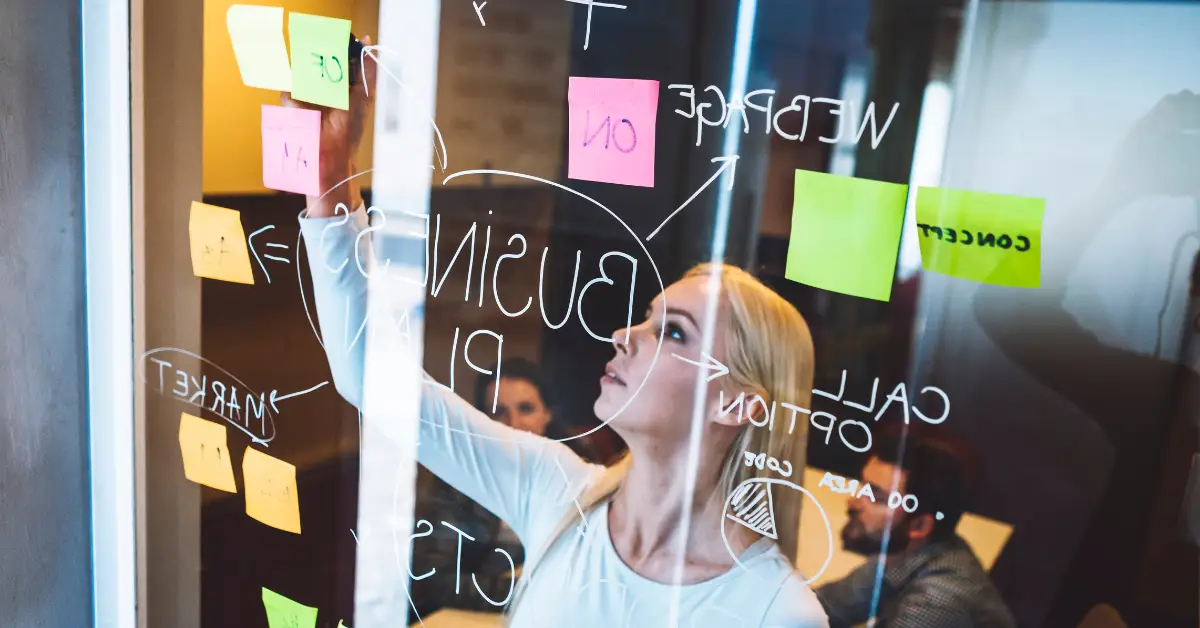 Young entrepreneur brainstorming startup ideas on a glass wall filled with sticky notes and flow diagrams.