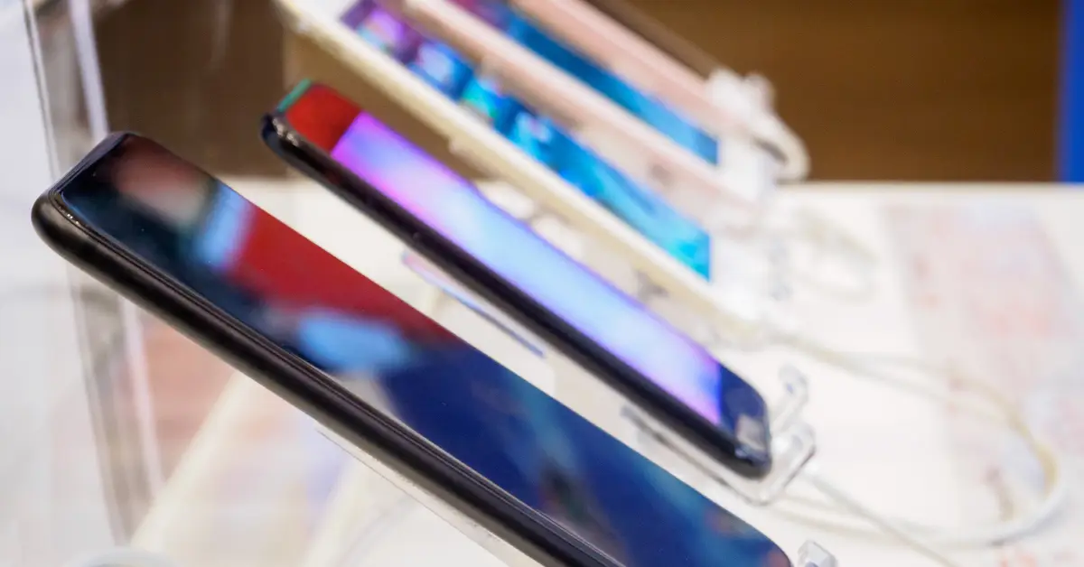 Row of smartphones on display, showcasing various models with vibrant screen colors.