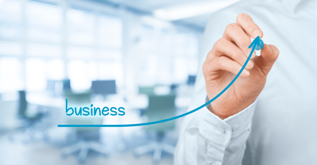 Person drawing an upward trend line labeled 'business' over a blurred office background.