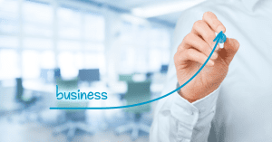 Person drawing an upward trend line labeled 'business' over a blurred office background.