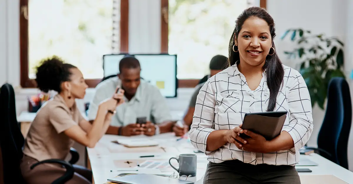 Confident female entrepreneur with a digital tablet, leading a diverse team in a bright office setting.