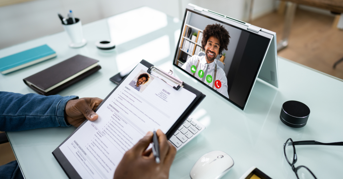 Person reviewing a resume while conducting an online video interview with a smiling candidate.