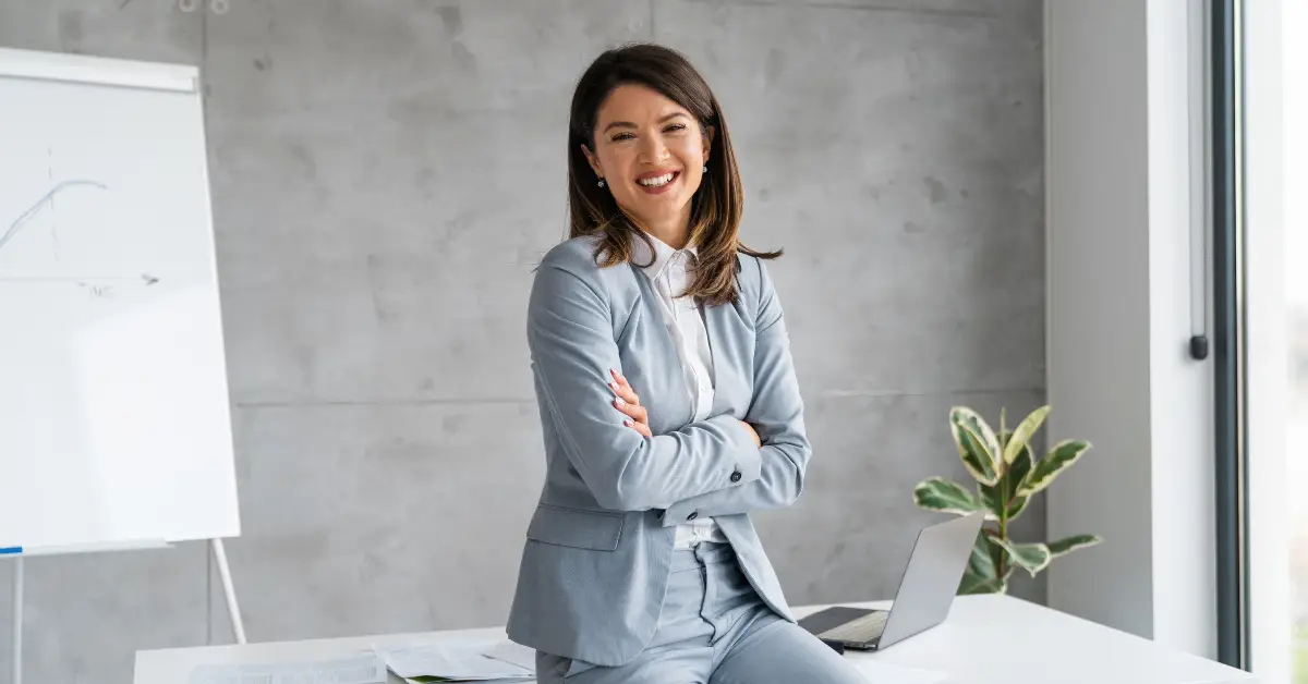 Confident businesswoman smiling in a modern office setting with a whiteboard in the background.