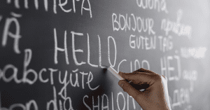 Hand writing 'Hello' in multiple languages on a chalkboard