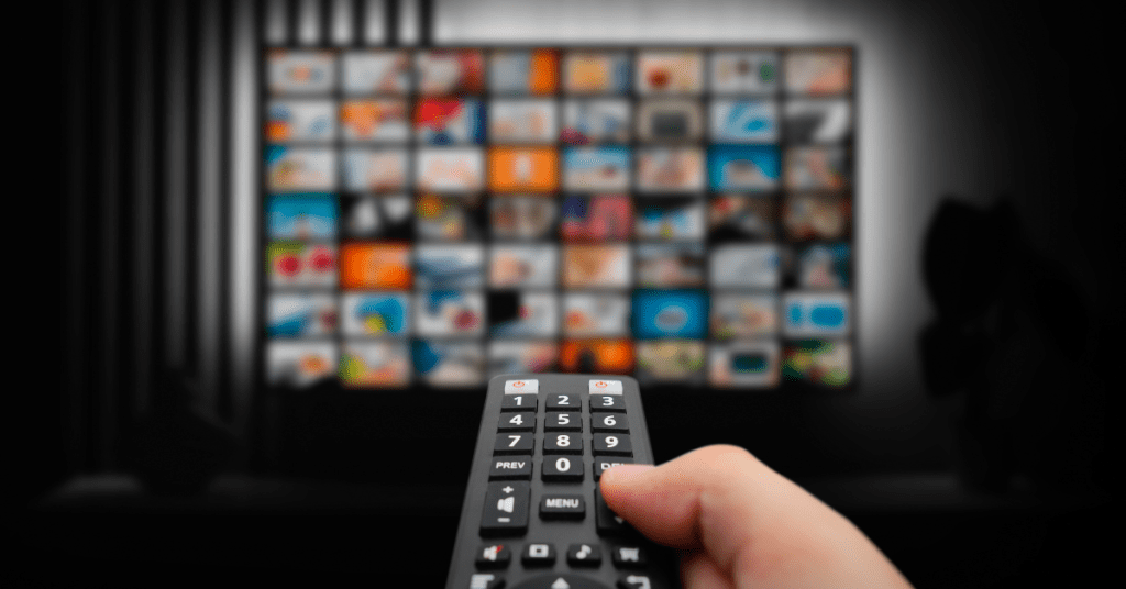 A person holding a remote control, pointing towards a screen displaying a variety of colorful streaming app icons.