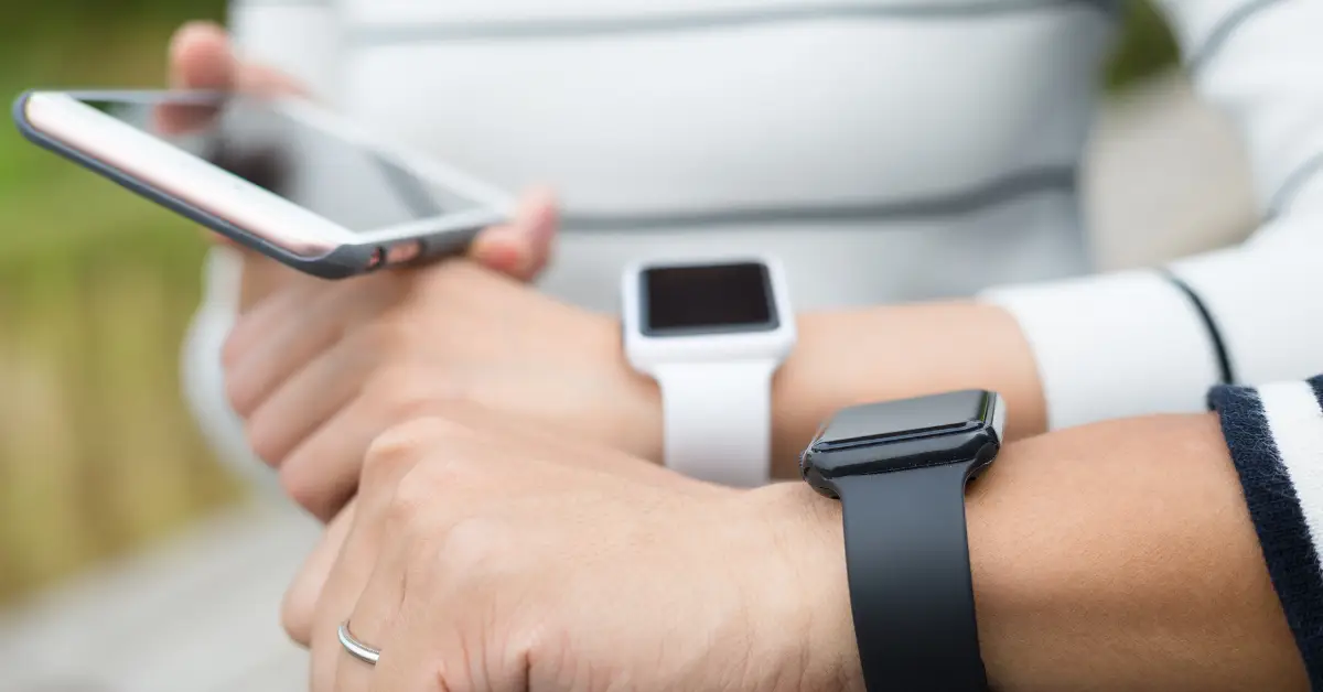 Person using a smartphone and wearing multiple smartwatches on both wrists, showcasing wearable health technology.