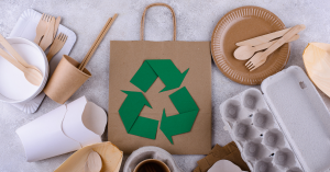 Assorted eco-friendly packaging materials including compostable utensils and recycled paper products with a recycling symbol.