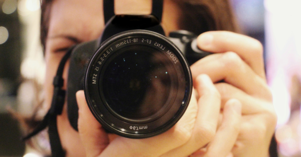 Photographer holding a digital camera, focusing through the lens.