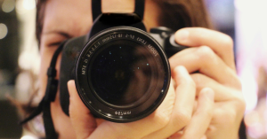Photographer holding a digital camera, focusing through the lens.
