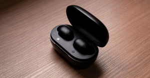 Black wireless earbuds in an open charging case on a wooden surface.