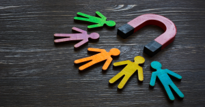 Colored wooden figures drawn towards a magnet on a wooden background.
