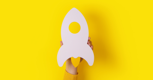 Hand holding a paper rocket symbolizing startup growth and acceleration against a bright yellow background.